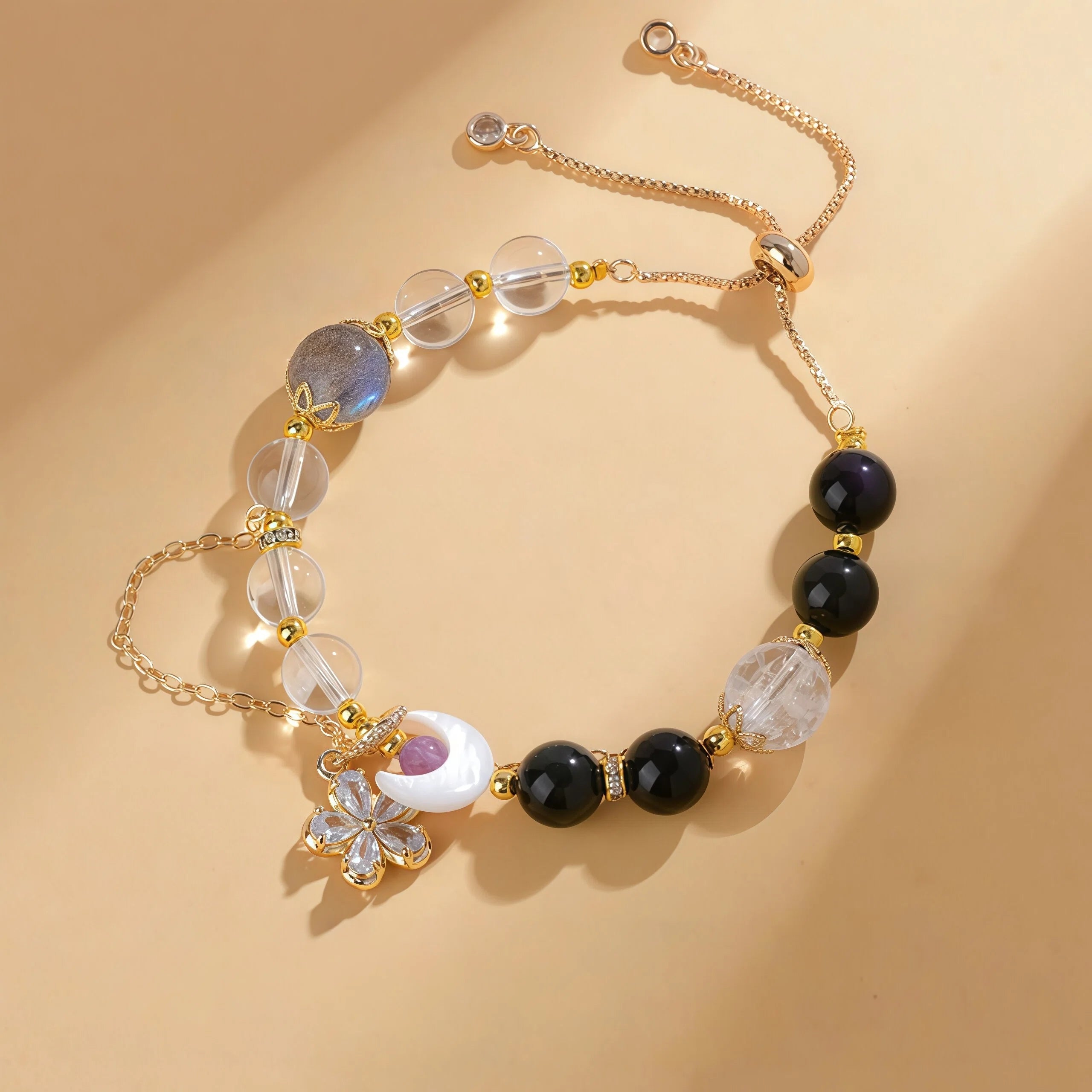 Gemini Zodiac Bracelet featuring 10mm Gray Moonstone, 8mm Obsidian, and 10mm Flower Quartz. Gold adjustable healing crystal jewelry for clarity with 8mm Clear Quartz and 5mm Amethyst accents - Kosmos Zen