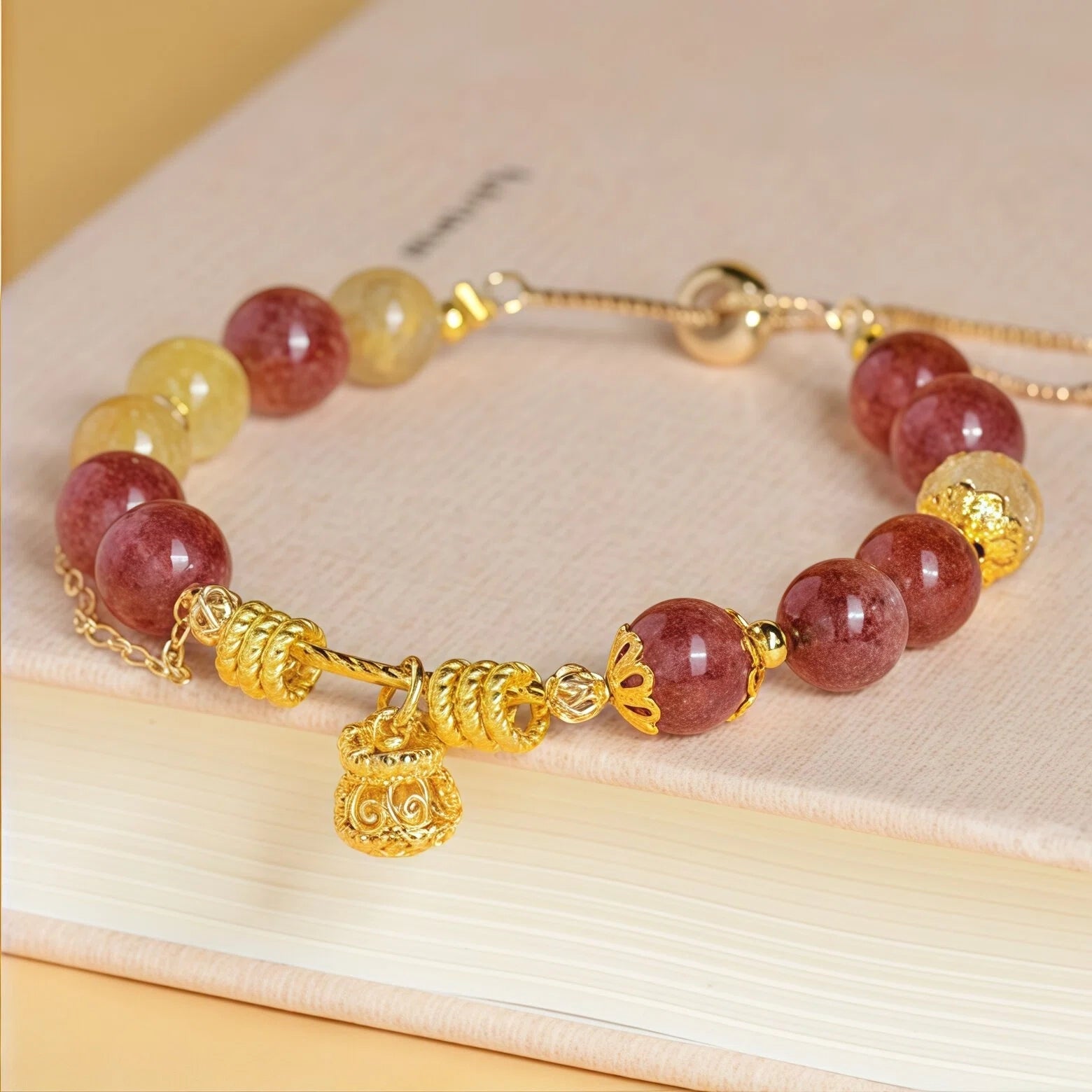 Styled flat lay of Leo Zodiac Bracelet resting on a book. Featuring 8mm Golden Rutilated Quartz and Strawberry Quartz beads with a gold Money Bag charm for wealth and love - Kosmos Zen