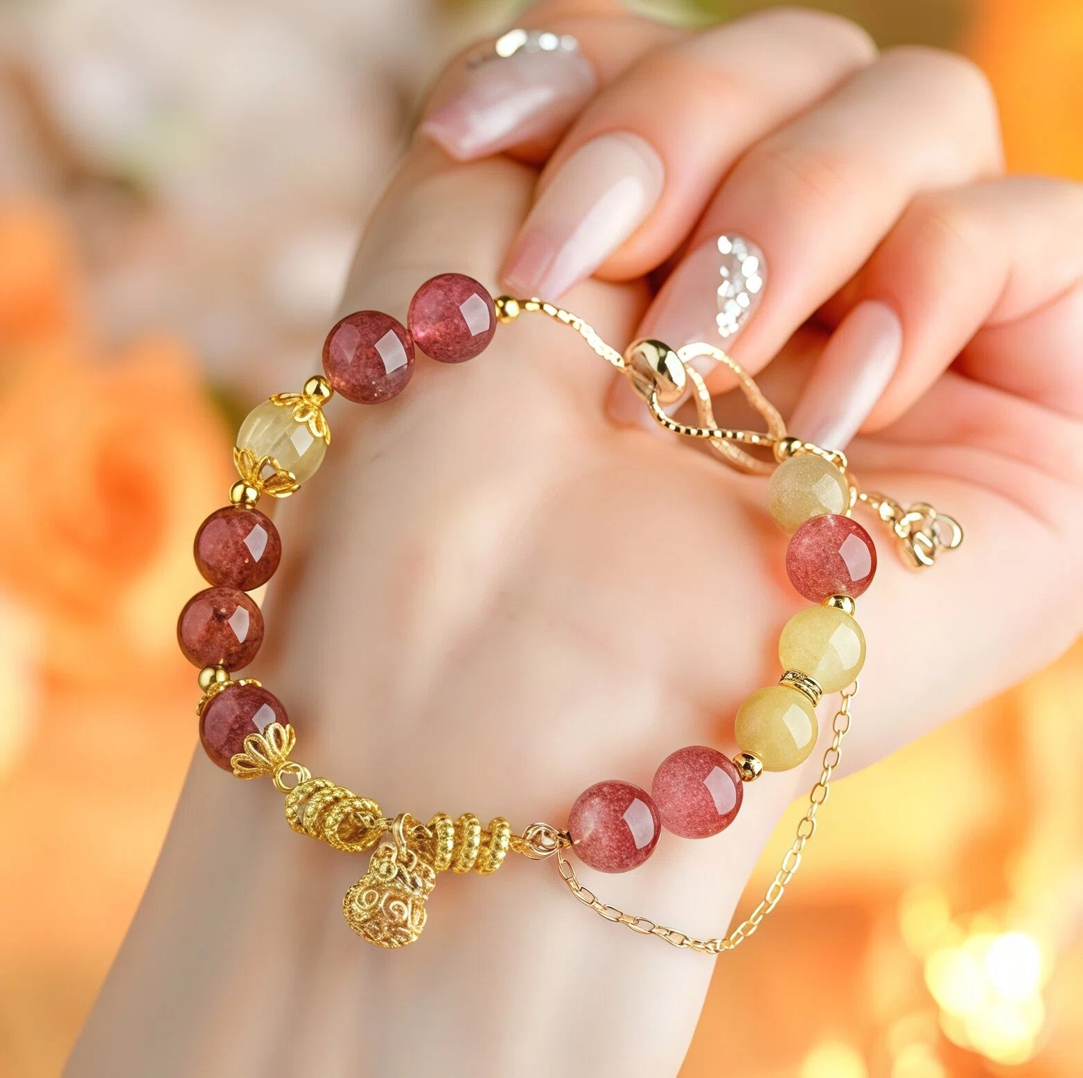 Hand holding Leo Zodiac Bracelet featuring 8mm Strawberry Quartz and Golden Rutilated Quartz beads. Close-up detail of gold Money Bag charm for wealth and love - Kosmos Zen
