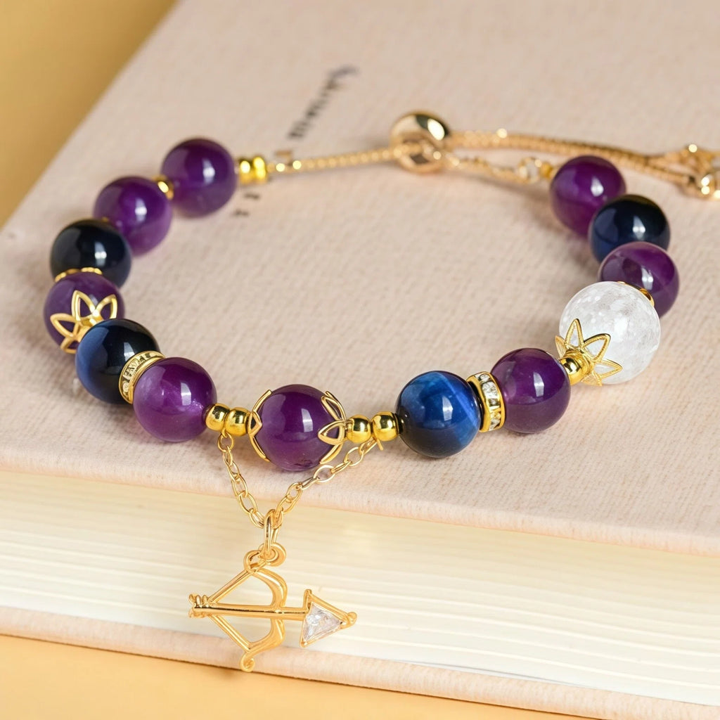 Styled flat lay of Sagittarius Zodiac Bracelet resting on a book. Featuring Blue Tiger Eye, Amethyst, and Flower Quartz beads with a gold Bow and Arrow charm for truth and adventure - Kosmos Zen
